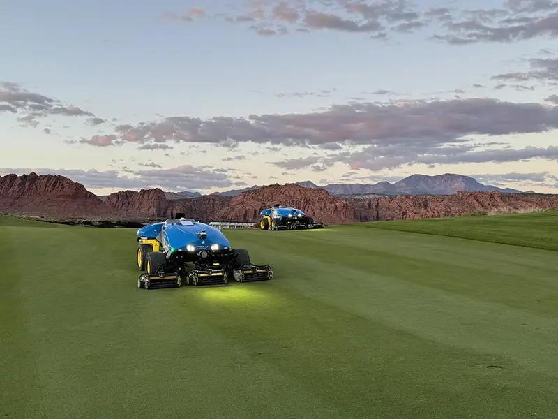 Two autonomous mowers cutting a golf fairway at dusk